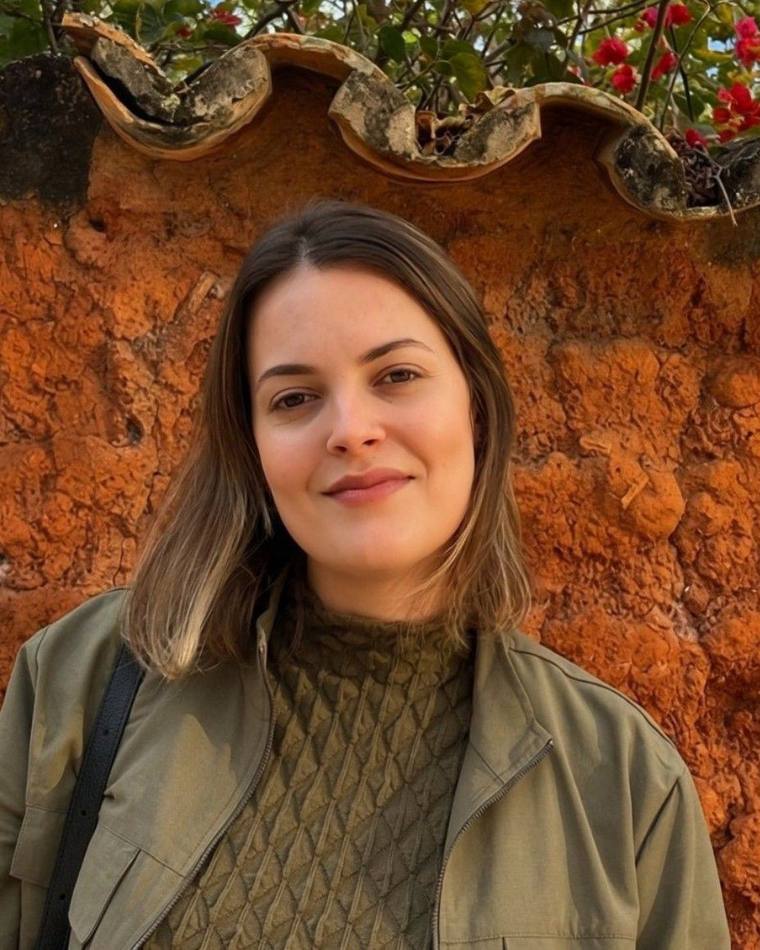 Júnnia Moreira, psicóloga, diante de um muro de terra com flores